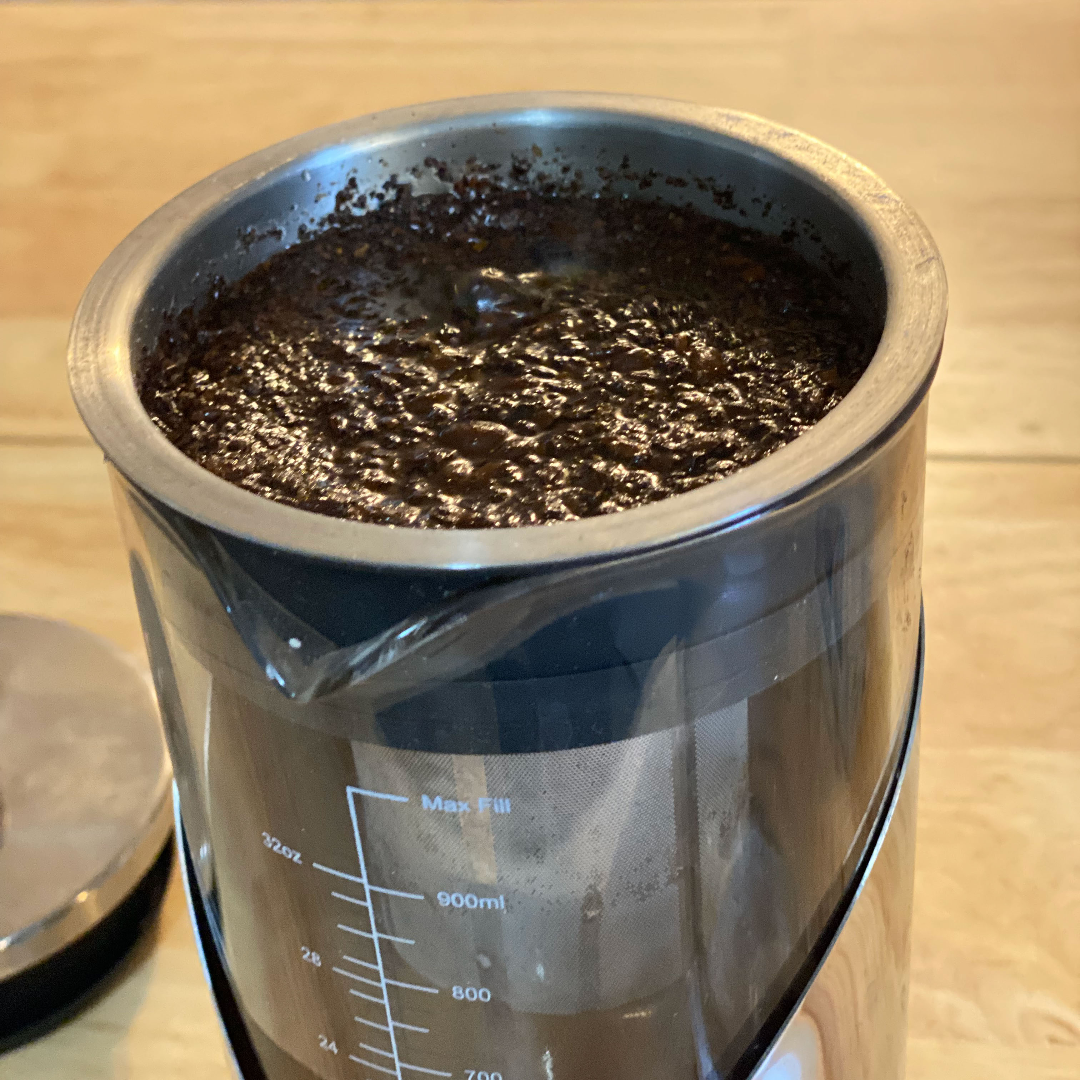 Metal and glass pitcher with blooming coffee grounds 